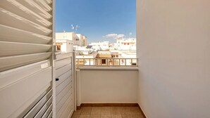 Un balcón con vista a edificios cercanos, una puerta blanca y un suelo de baldosas.