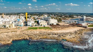 An aerial view of a coastal town with buildings, a rocky shoreline, and clear blue waters. - Apartment 'Grande Struttura - Matrimoniale 1' with Balcony, Wi-Fi and Air Conditioning (Torre San Giovanni)