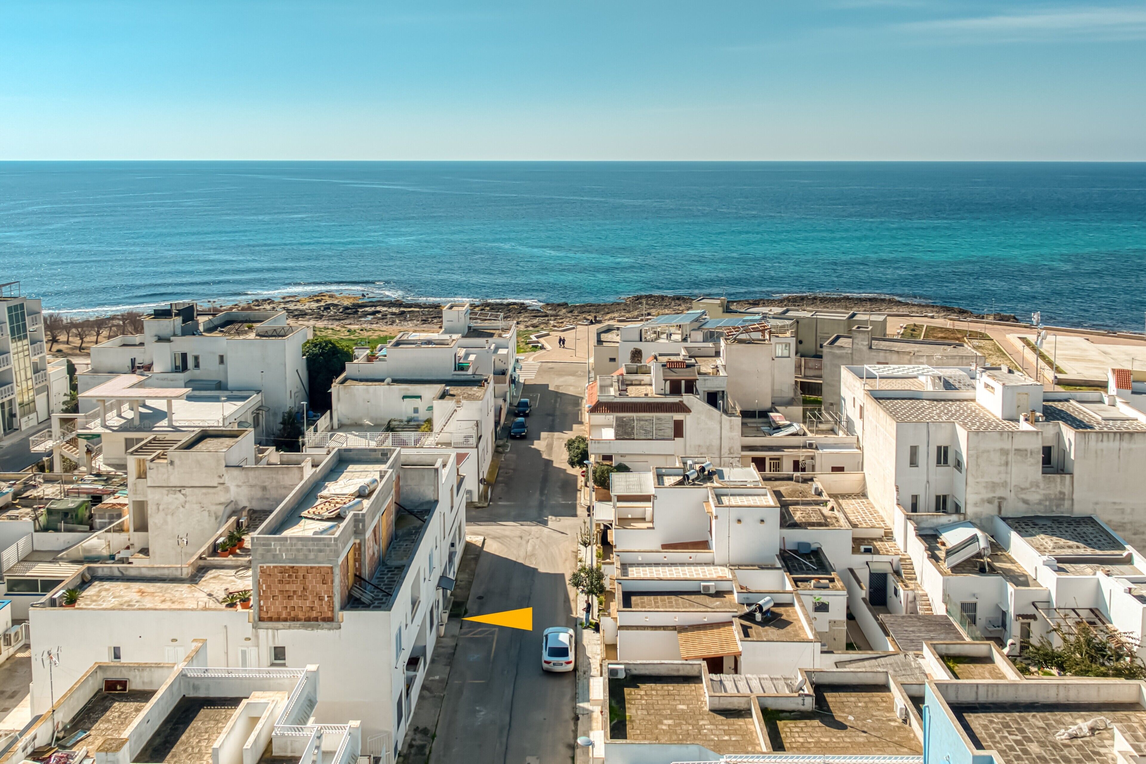 Una località costiera con edifici bianchi, vista libera sul mare e una stretta via.