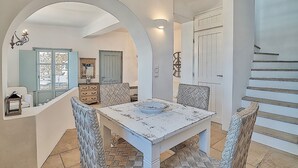 A dining area with a white table and chairs, a mirror, and a staircase. - Villa 'Afroditi A' with Sea View, Wi-Fi and Air Conditioning (Antiparos Town)
