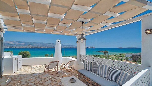 A covered outdoor seating area with a stone floor, a white column, and a view of the sea. - Villa 'Afroditi A' with Sea View, Wi-Fi and Air Conditioning (Antiparos Town)