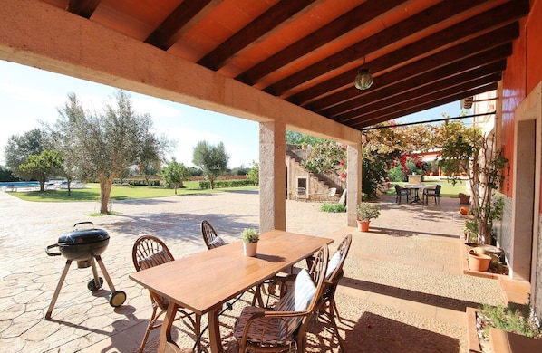An outdoor patio with a wooden table and chairs, a barbecue grill, and potted plants.