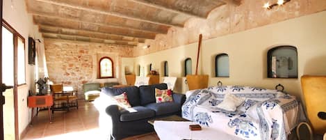 A rustic room with stone walls, a wooden ceiling, a sofa, a bed with patterned bedding, and a small table.