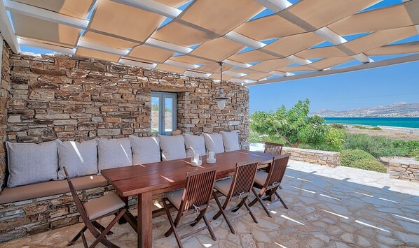 A stone wall with a window, a wooden table with chairs, and a view of the sea. - Villa 'Afroditi B' with Sea View, Wi-Fi and Air Conditioning (Antiparos Town)