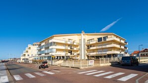 Un edificio a più piani con balconi, un attraversamento pedonale e un veicolo parcheggiato.