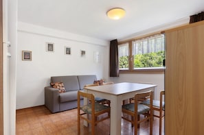 Une pièce comprenant un canapé, une table à manger avec des chaises, une fenêtre avec des rideaux et des tableaux encadrés accrochés au mur.