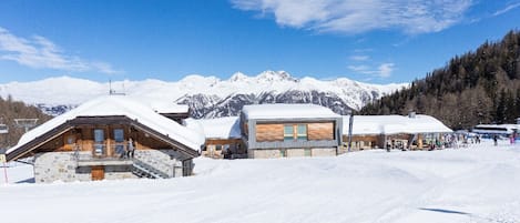 A snow-covered lodge with wooden architecture, a ski lift in the background, and a mountain range.