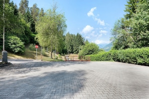 Un chemin pavé mène à un panneau de signalisation, et il est bordé d’une végétation luxuriante et d’arbres.