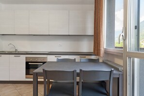 Une cuisine moderne avec des meubles blancs, un four encastré et un coin repas comprenant une table et des chaises.