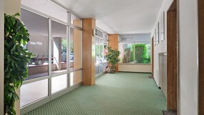 A corridor with large windows, a green carpet, wooden columns, and potted plants. - Apartment 'Marilleva 900 Kristall' with Mountain View, Shared Terrace and Wi-Fi (Mezzana)