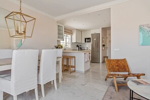 A modern kitchen with white cabinetry, a central island, and a dining area with white chairs. - Holiday Home 'Cecilia' with Sea View, Wi-Fi and Air Conditioning (Nerja)