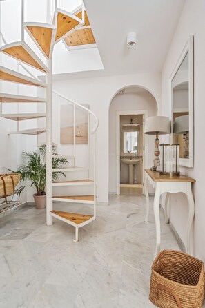 A spiral staircase with wooden steps and white railings, a potted plant, a wicker basket, and a mirror on a console table. - Holiday Home 'Cecilia' with Sea View, Wi-Fi and Air Conditioning (Nerja)