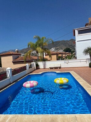 A swimming pool with two inflatable rings, a white building, and a mountain in the background. - Holiday Home 'Cecilia' with Sea View, Wi-Fi and Air Conditioning (Nerja)