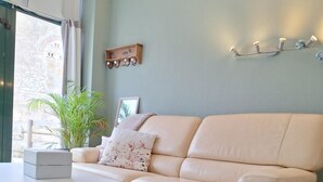 Un salon avec un canapé beige, une table basse en bois, un tapis bleu, une plante en pot et un luminaire fixé au mur.