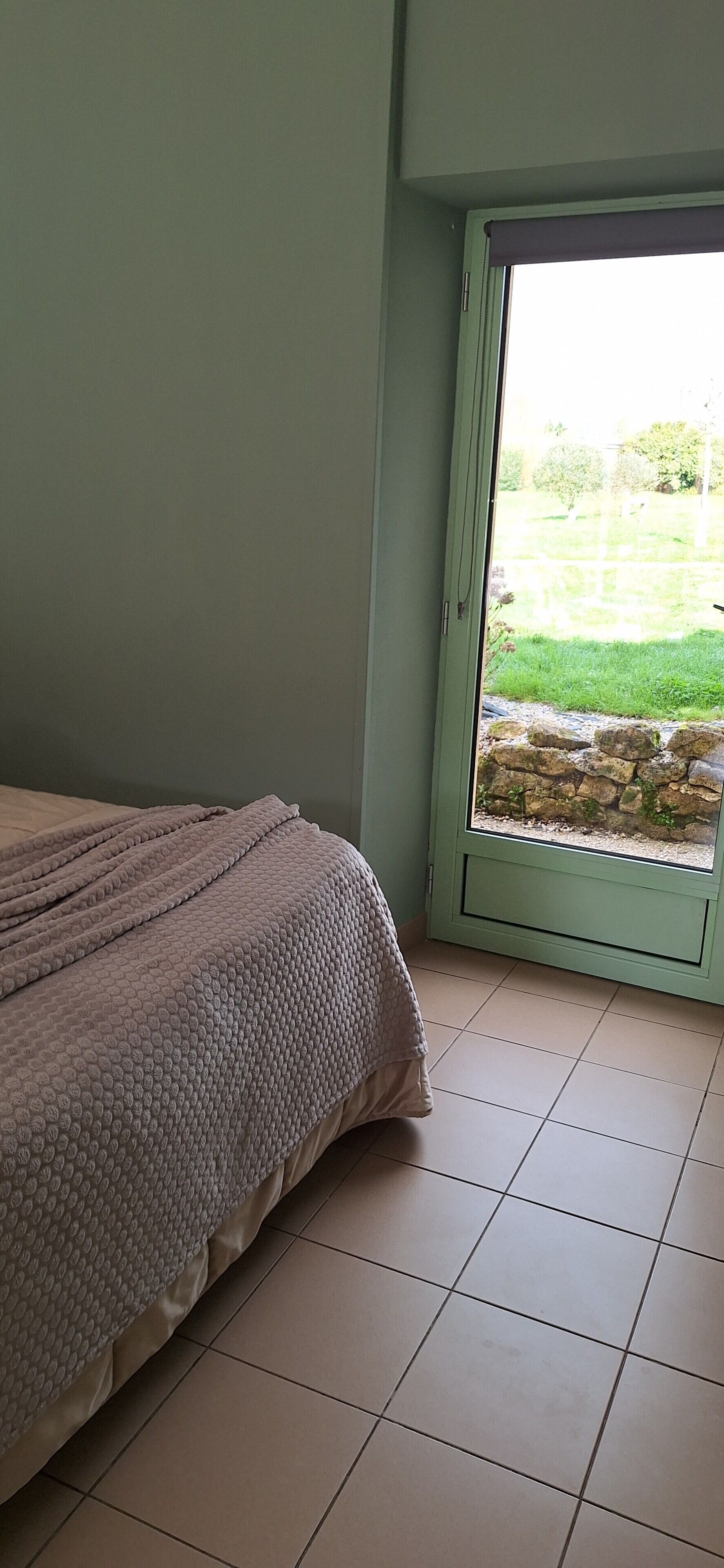 A bedroom with a bed, a window, and a view of a garden.