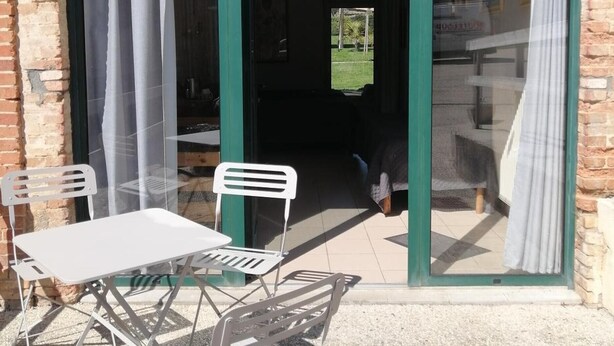 Une terrasse avec une table et des chaises, un mur en briques et une grande porte vitrée avec des rideaux.
