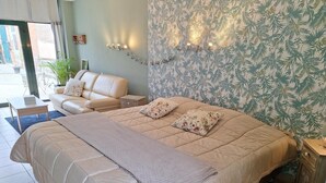 Une chambre avec un grand lit, un canapé, une petite table et un mur orné d’un motif végétal.