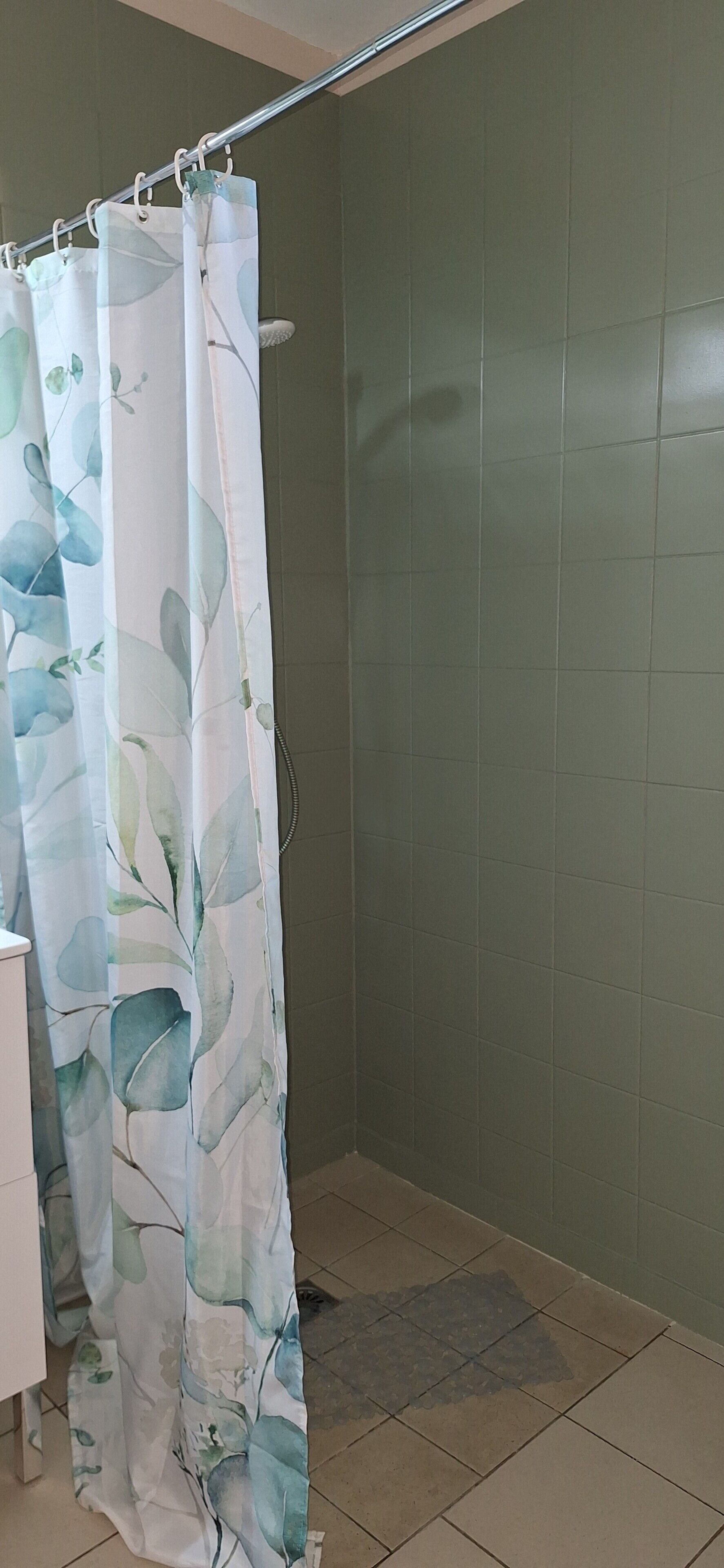 A shower area with a curtain featuring a leaf pattern, a showerhead, and tiled walls.
