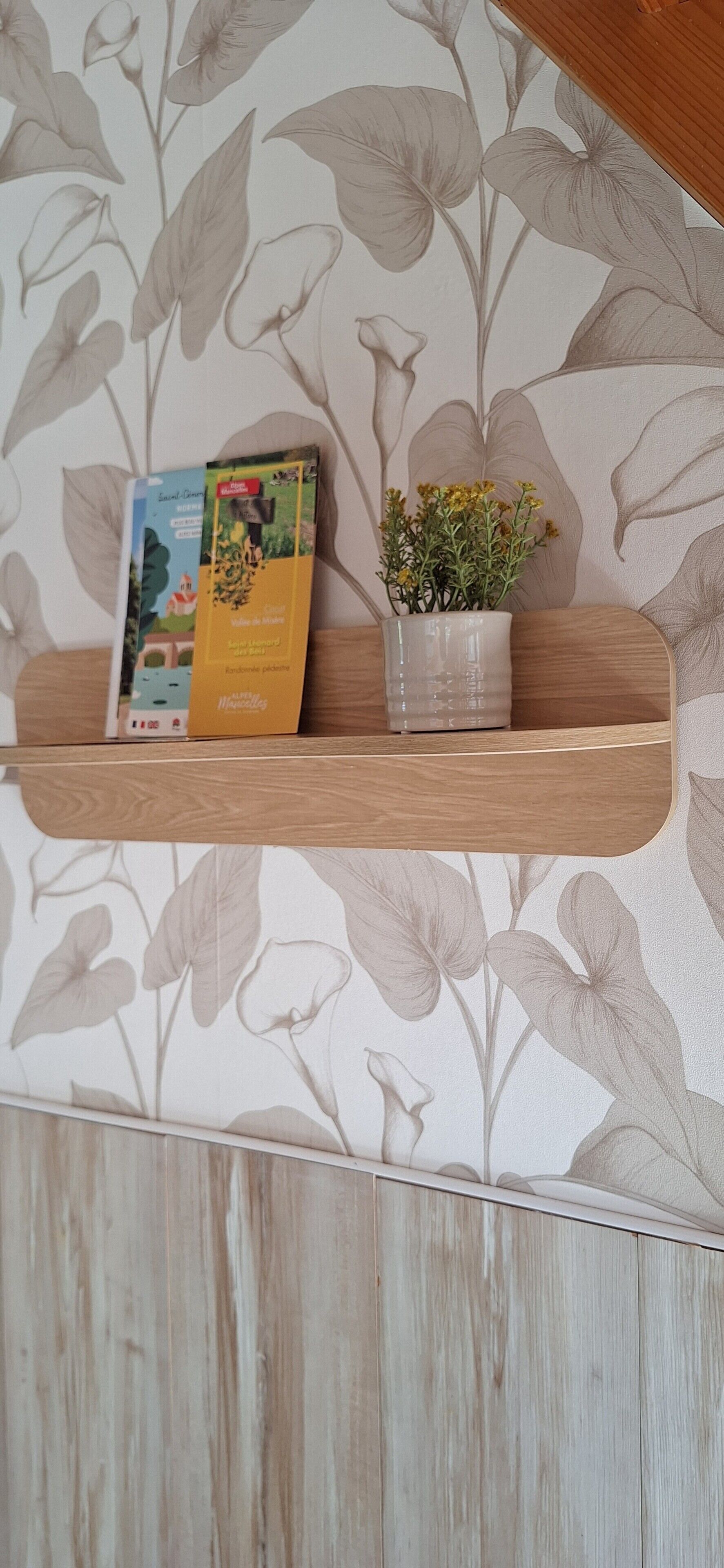 A shelf with a book and a potted plant against a floral wallpaper.