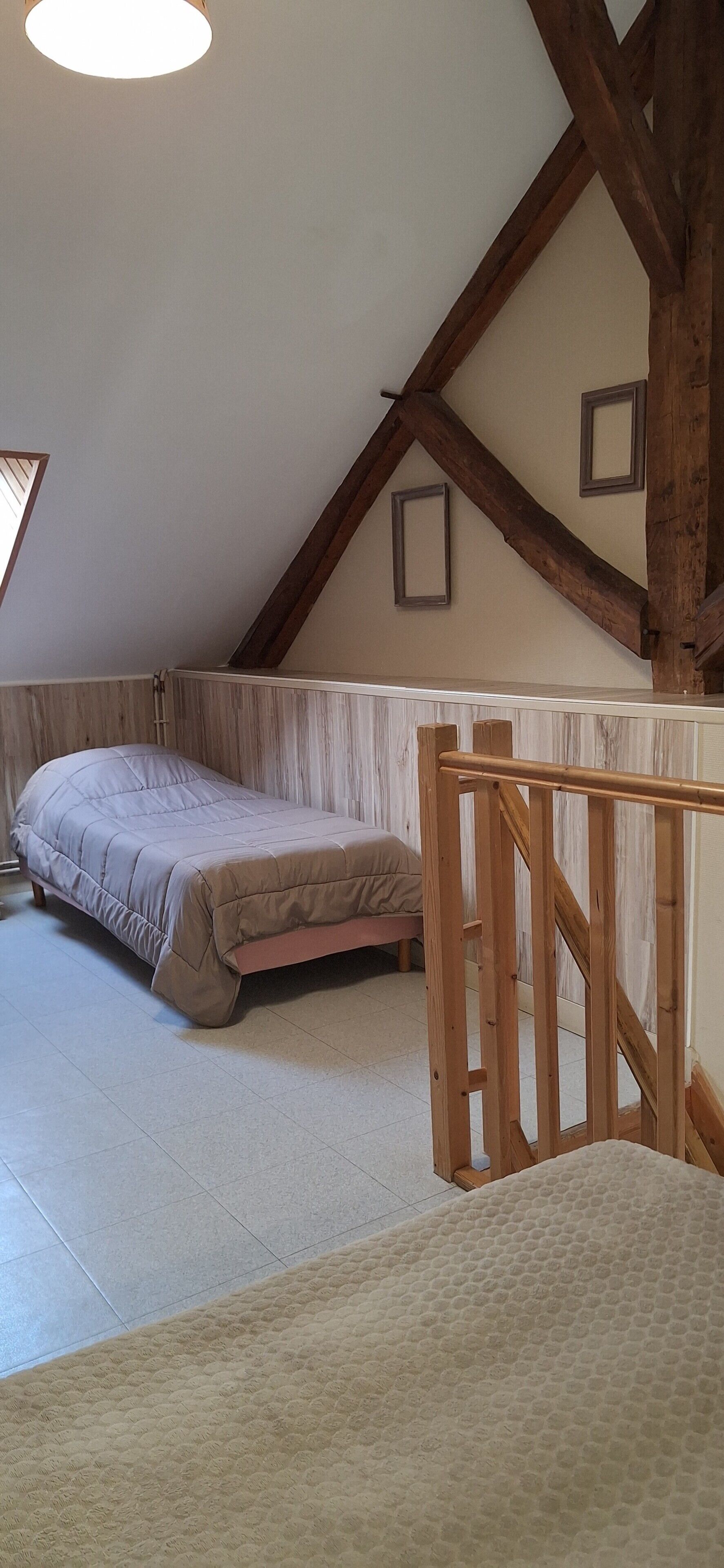 Un dormitorio con techo inclinado, vigas de madera, una cama y una ventana pequeña.