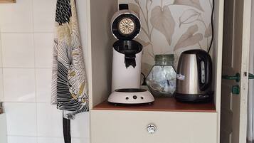 A kitchen area with a microwave, coffee maker, kettle, and a wine bottle on a shelf.