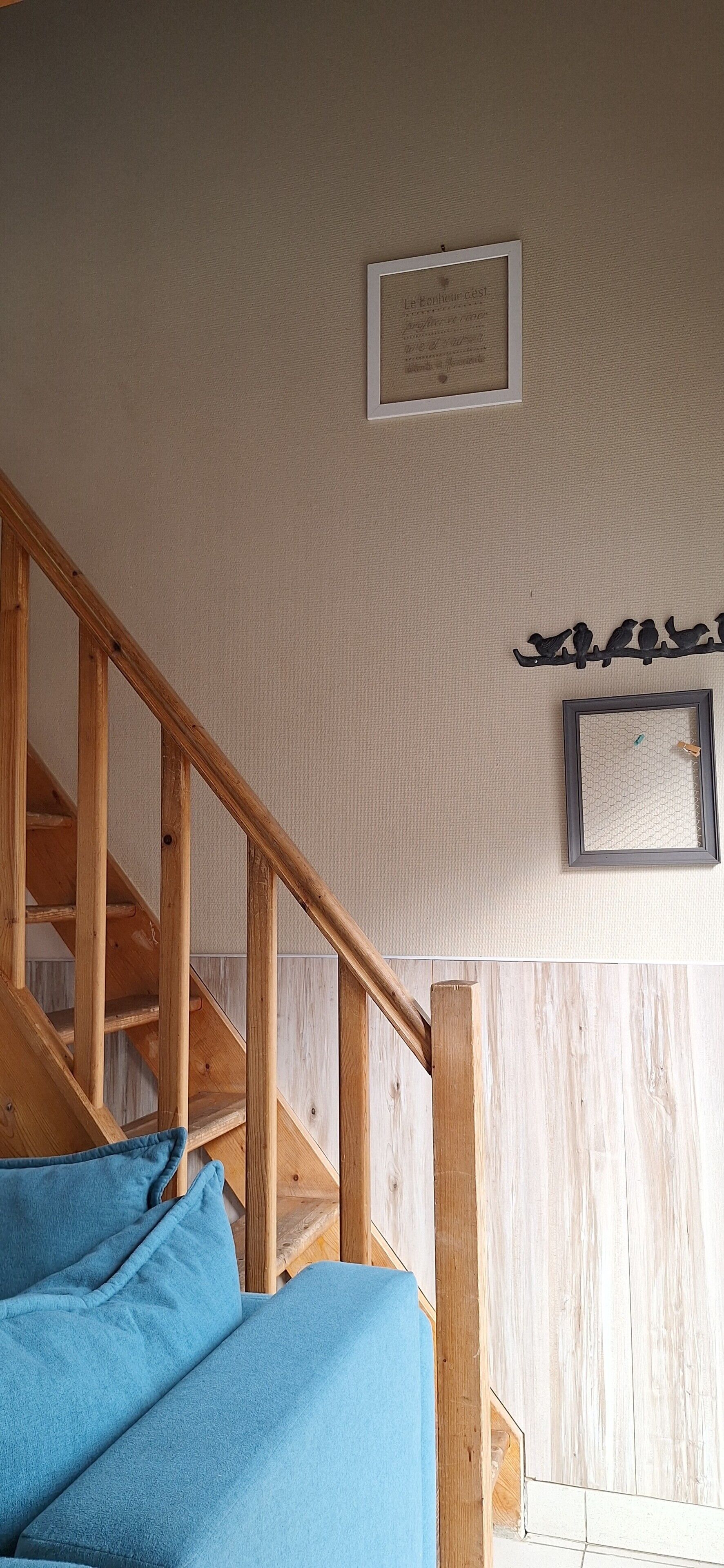 A staircase with wooden railings, a blue cushion, a framed picture, and a wall-mounted bird decoration.