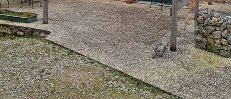 A building with a brick facade, two arched doorways, a gravel driveway, and a wooden bench.