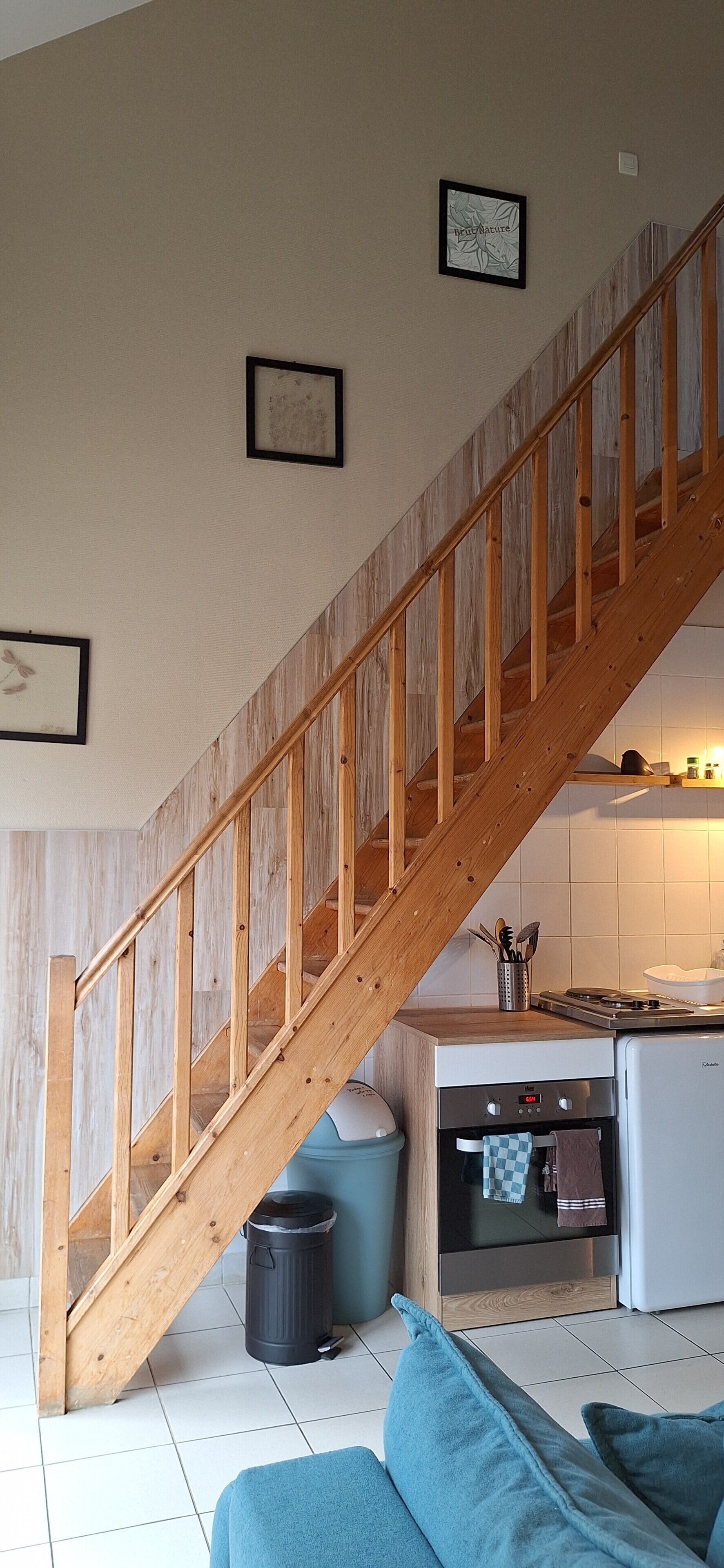 A wooden staircase leading to a kitchen area with a stove, oven, and a trash bin.