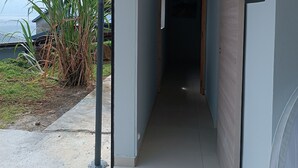 A narrow hallway with a view of the outdoors, including a plant and a building in the distance. - O'Romarin | Sea & rivers - Chutes du Carbet (Capesterre-Belle-Eau)