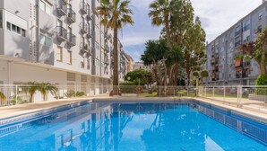 A swimming pool with a tiled deck, surrounded by apartment buildings with balconies and palm trees. - Apartment 'La Siesta 5' with Shared Pool, Wi-Fi and Air Conditioning (Fuengirola)