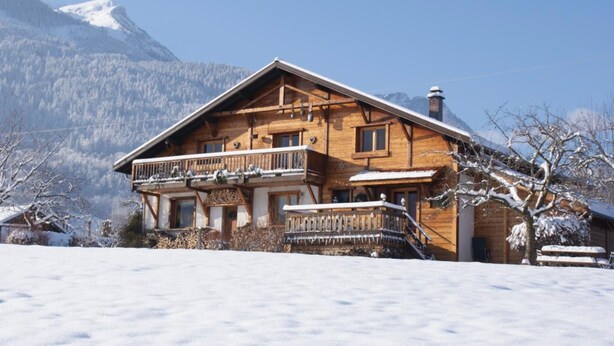 Eine Holzhütte mit Balkon vor einer verschneiten Bergkulisse.