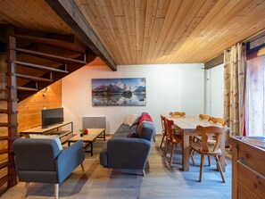 Un accogliente interno di una baita con una scala in legno, un divano, un tavolo da pranzo e un quadro di un paesaggio montano.