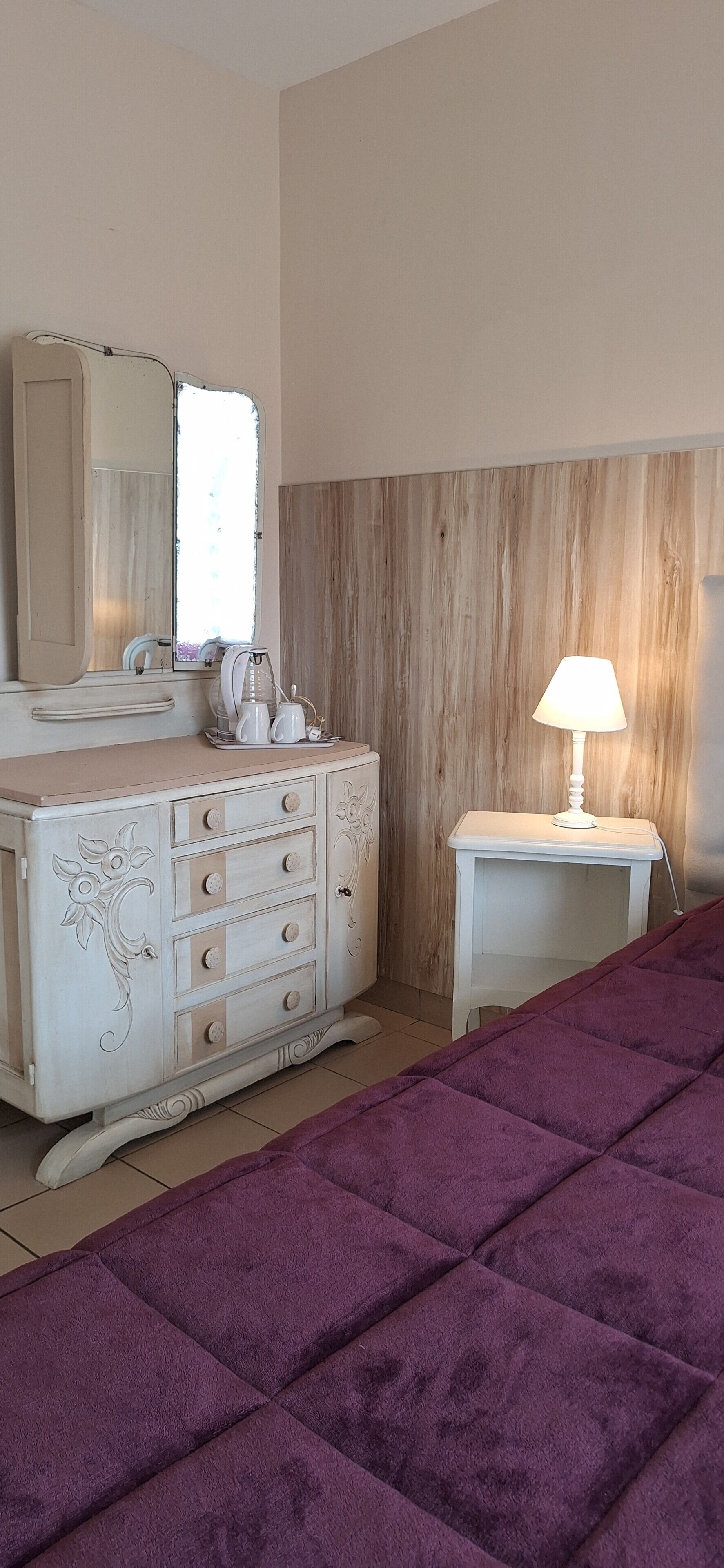 Een slaapkamer met een bed, een dressoir met lades, een spiegel, een lamp en een raam.