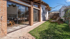 Uma casa com varanda, uma cadeira de balanço de madeira e uma porta de vidro que dá para uma sala de jantar.