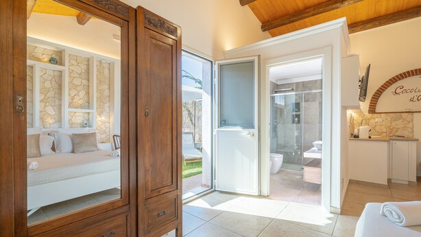 Quarto com armário de madeira, cama, banheiro com porta de vidro e cozinha.