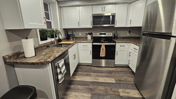A modern kitchen with white cabinets, stainless steel appliances, a granite countertop, and a herringbone-patterned wood floor. - Bright New 1 bedroom Retreat (Candler)
