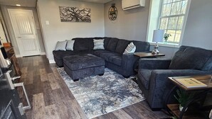 A modern living room with a sectional sofa, a small table, and a window with a view. - Bright New 1 bedroom Retreat (Candler)