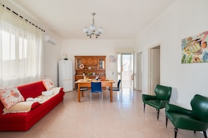 A living room with a red sofa, a wooden dining table, and green chairs.