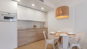 Una cucina moderna con mobili bianchi, forno a incasso, piano di lavoro in legno e zona pranzo con tavolo rotondo e sedie bianche.