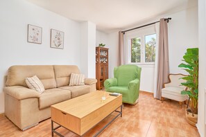 A living room with a beige sofa, a green armchair, a wooden coffee table, and a cabinet. - Apartment 'Los Cactus' with Balcony, Wi-Fi and Air Conditioning (Almuñécar)