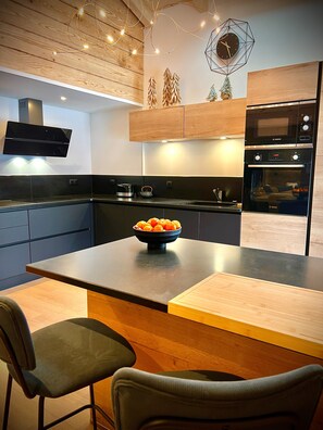 Une cuisine moderne dotée d’un îlot central en bois, d’appareils électroménagers de la marque Bosch et d’une horloge décorative.