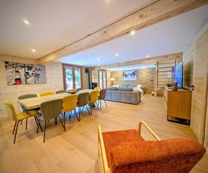 Een ruime kamer met een houten plafond, een eethoek met een tafel en stoelen, een bank en een televisie.