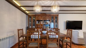 A dining room with a wooden table, chairs, a chandelier, a cabinet with glass doors, and a television on the wall. - Country House 'Casa Da Carballeira' with Mountain View, Private Garden and Wi-Fi (A Estrada)
