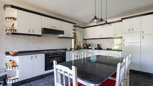 A modern kitchen with white cabinets, a granite countertop, and a dining table with white chairs. - Country House 'Casa Da Carballeira' with Mountain View, Private Garden and Wi-Fi (A Estrada)