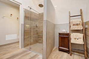 A modern bathroom with a glass shower enclosure, a wooden ladder with towels, and a wooden cabinet.