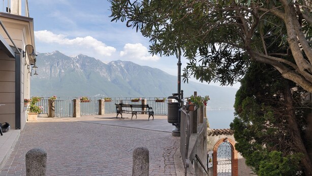 Eine gepflasterte Terrasse mit einer Bank, einem Metallzaun und Blick auf die Berge.