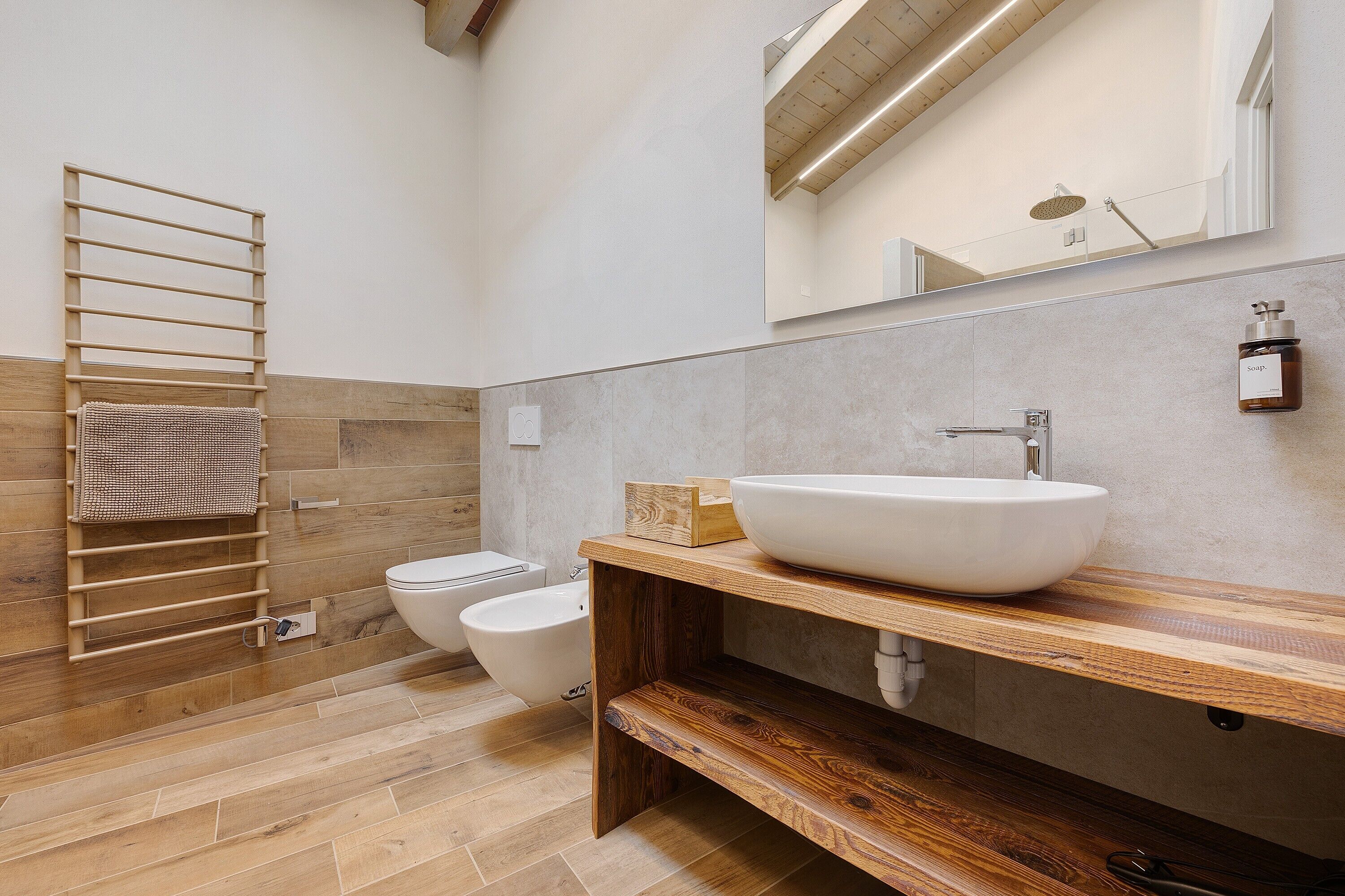 Un baño moderno con un mueble de tocador de madera, un espejo grande, un perchero para toallas y un bidé.