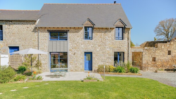 A stone building with a grey roof, a blue door, and a patio area with a table and chairs. - Holiday Home 'La Ferme D'Alcide' with Private Terrace, Private Garden and Wi-Fi (Québriac)