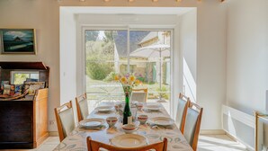 A dining area with a table set for four, a wooden cabinet, and a painting on the wall. - Holiday Home 'La Ferme D'Alcide' with Private Terrace, Private Garden and Wi-Fi (Québriac)