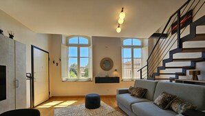 A modern living room with a sofa, ottoman, and a staircase.